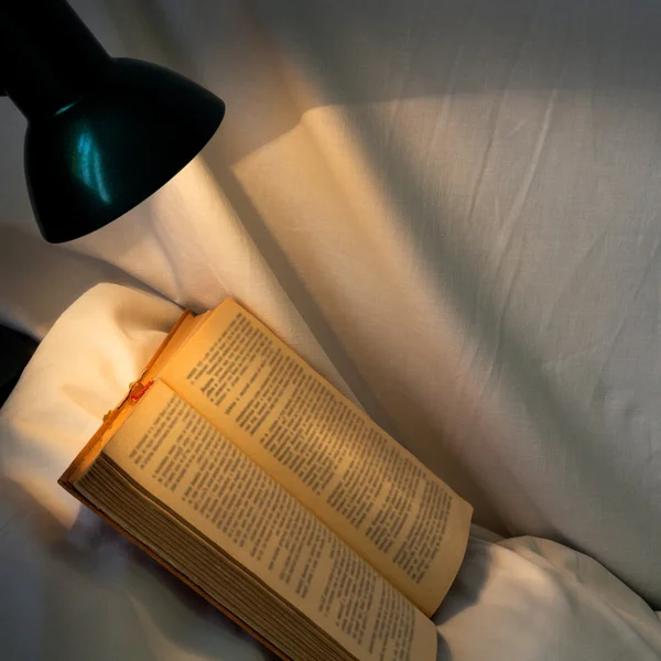 Book on white pillow lit table lamp