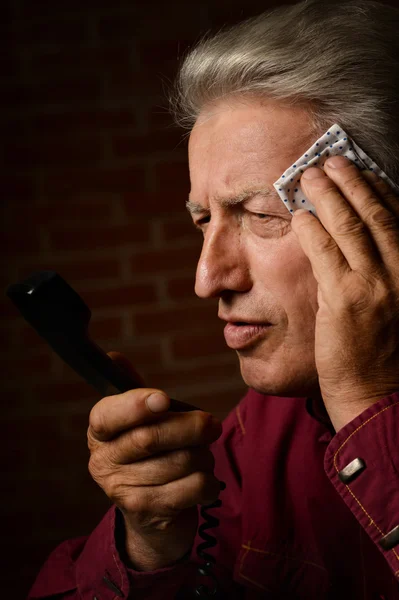 Sick mature man speaking on phone on a brick background