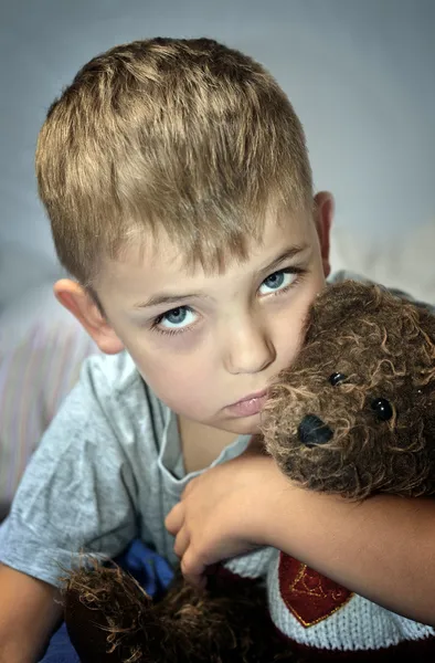 Small sad boy with eye bruise and teddy bear