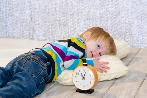 Tired toddler lying down with alarm clock in front