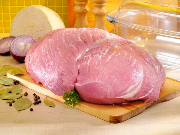 Raw pork ham on kitchen cutting board with glass baking pan
