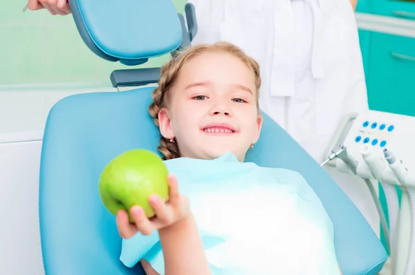 Girl in the dentist\'s chair shows a green apple