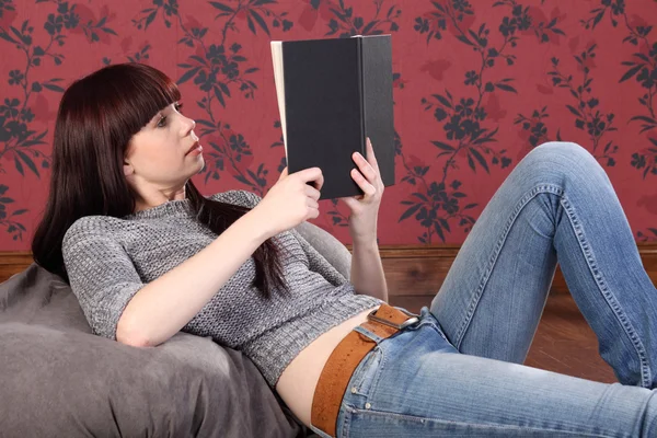 Pretty young woman lying on bean bag reading book