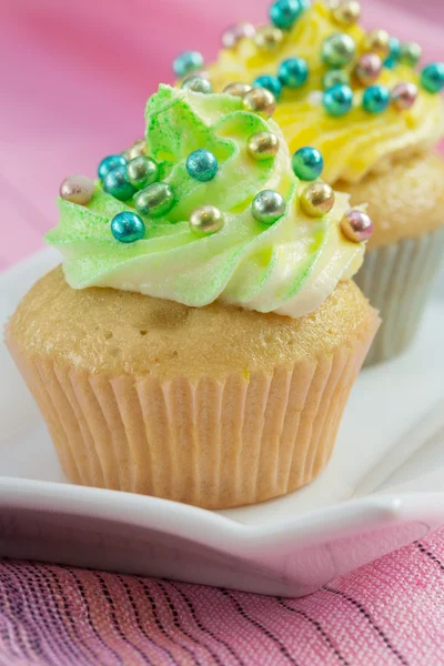 Two cupcakes with yellow and green buttercream and colorful de
