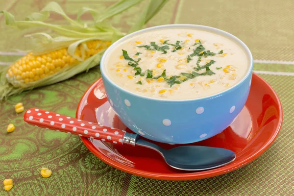 Cream of corn soup in blue bowl with fresh cob of corn on the si