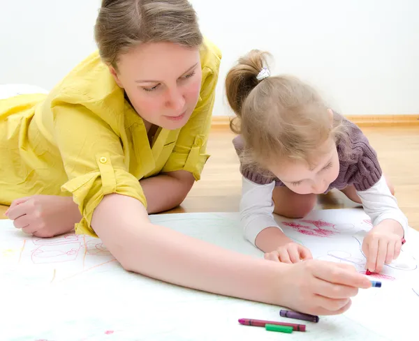 Young woman and little girl drawing together sitting on the floor