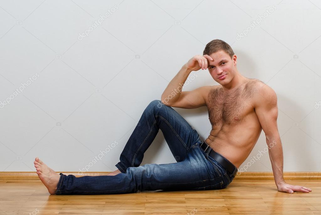 Handsome guy in jeans with bare torso sitting on the floor ...