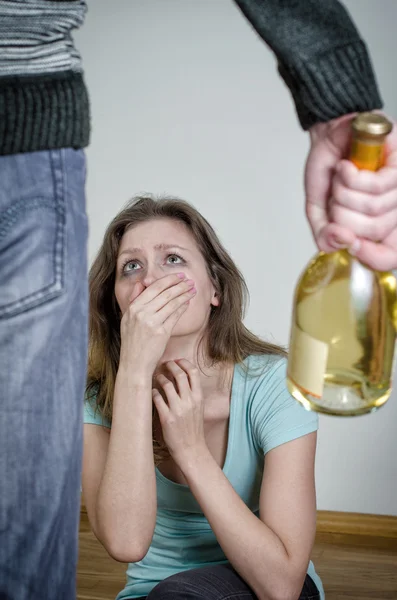 Home violence concept. Frightened woman and male hand holding bottle of wine