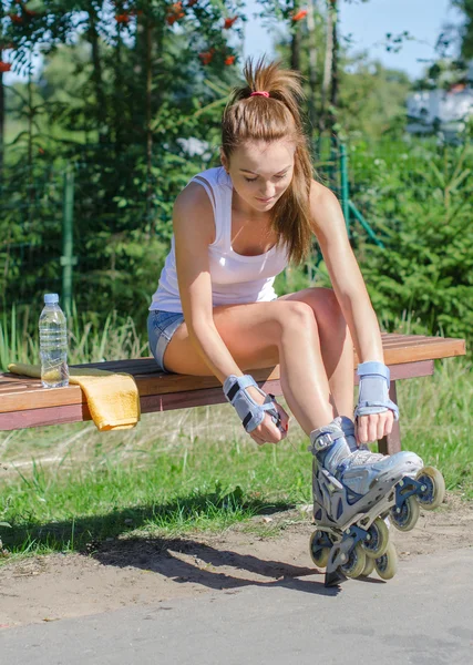 Pretty girl sitting on the bench and putting on inline skates.