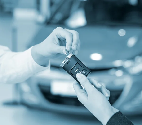 Female hand getting modern car key on a car background