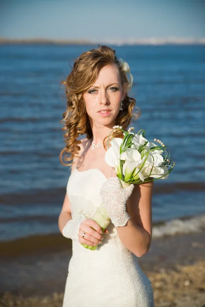 Beautiful bride with a bouquet of calla lilies on coast of river