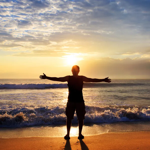 Man with his hands up on the dawn on the beach