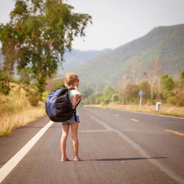 Little girl with backpack walking on the road