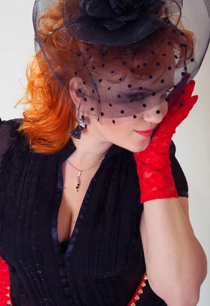 Young woman with red hair in black hat with net veil