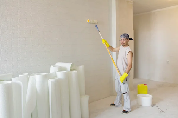 Young man with painting roller painting wallpaper
