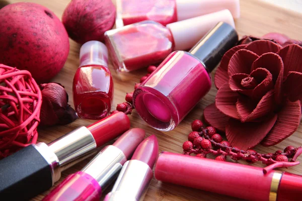 A collection of makeup: lipsticks, lip gloss and nail polishes decorated with red potpourri all in red and pink shades