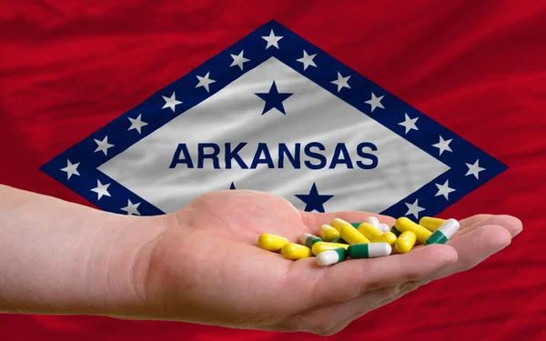 Holding pills in hand in front of arkansas us state flag