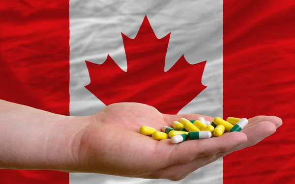 Holding pills in hand in front of canada national flag