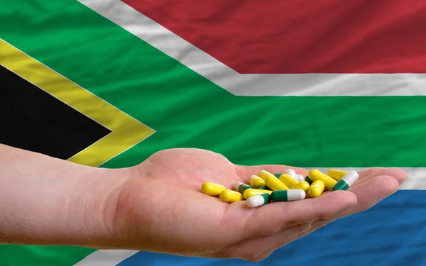 Holding pills in hand in front of south africa national flag