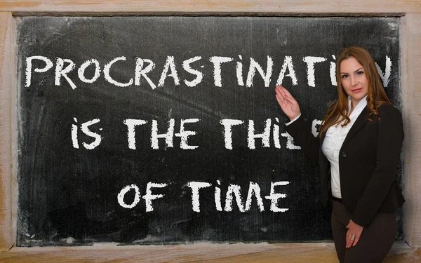Teacher showing Procrastination is the thief of time on blackboa