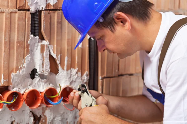 Worker installing electrical wires in building wall