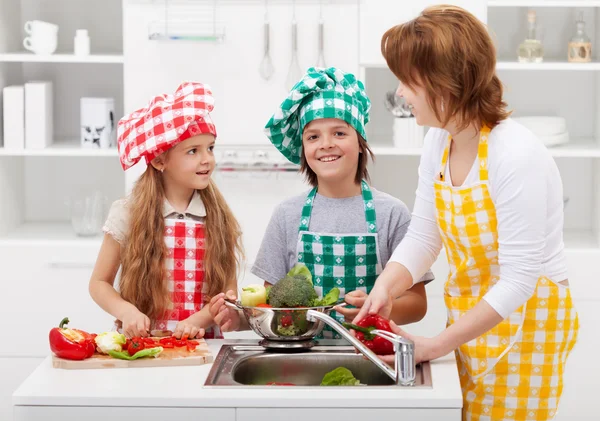 Woman and kids washing vegetables in the kitchen