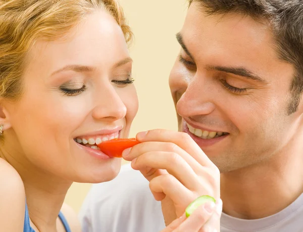 Cheerful young couple eating together tomatoes