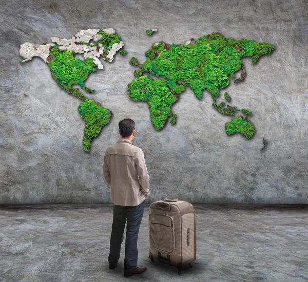 Young man standing and looking to green world map on cement wall with big suitcase use for people traveling theme
