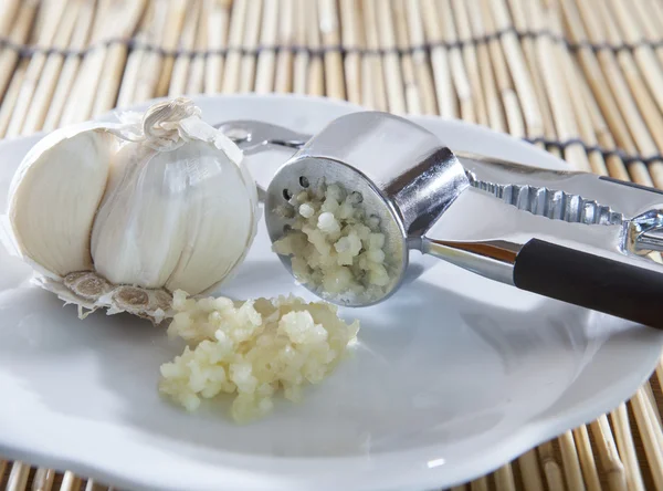 Fresh garlic crushed by garlic crusher on white dish on kitchen