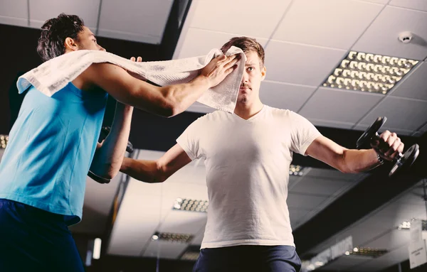 Young man wiping sweat off of friend's face in gym