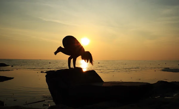 Silhouette yoga girl by the beach at sunrise doing Crane Pose