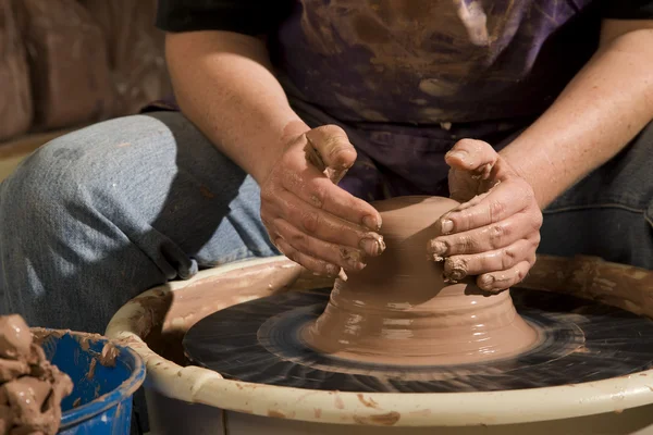 Hands forming clay on wheel