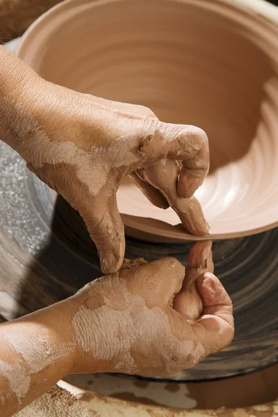 Hands forming clay on wheel