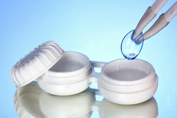 Contact lenses in containers and tweezers on blue background