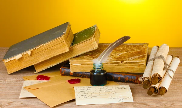 Old books, scrolls, feather pen and inkwell on wooden table on yellow background