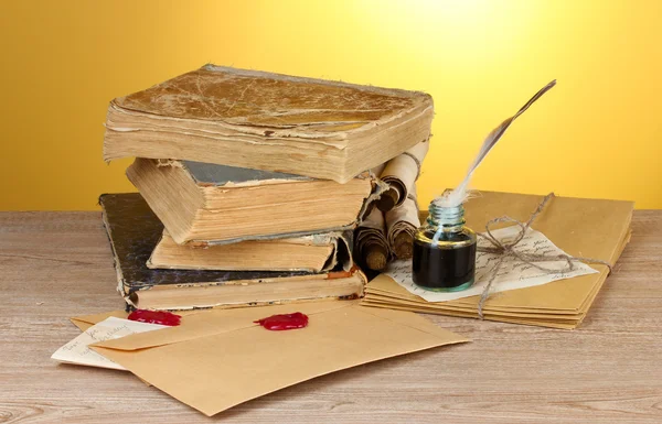 Old books, scrolls, feather pen and inkwell on wooden table on yellow background