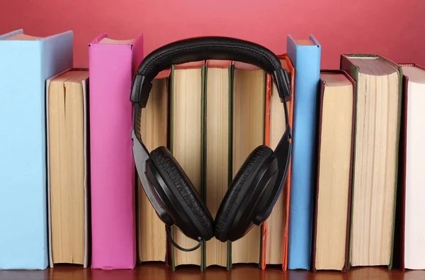 Headphones on books on wooden table on pink background