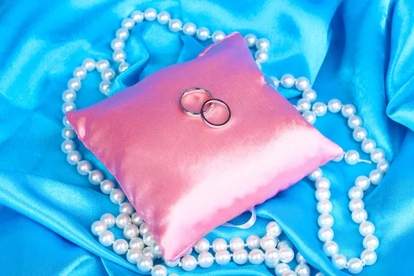 Wedding rings on satin pillow on blue cloth background