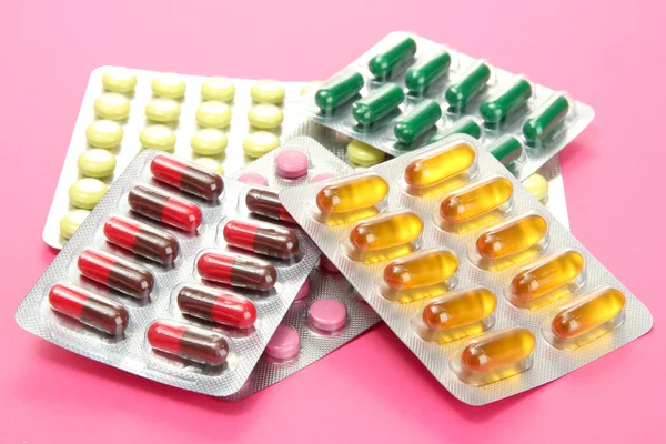 Capsules and pills packed in blisters, on pink background