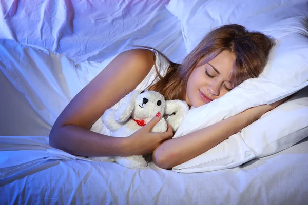 Young beautiful woman with toy rabbit sleeping on bed in bedroom
