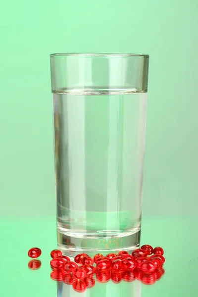 A glass of water and pills on green background close-up