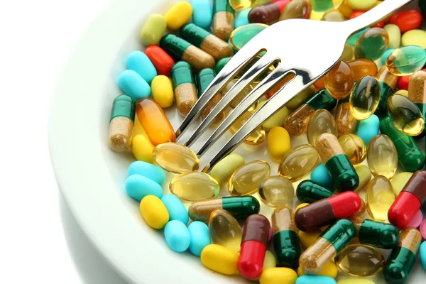 Colorful capsules and pills on plate with fork, isolated on white