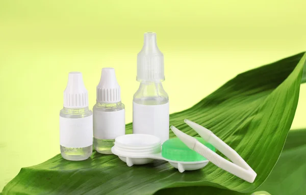 Eye drops and lenses on leaf on green background