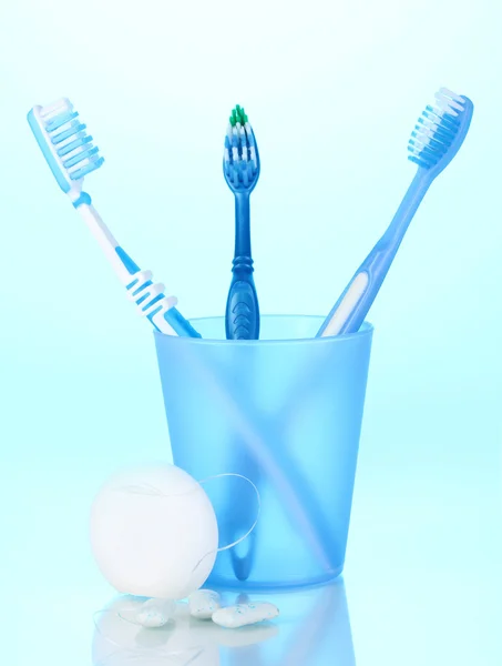 Toothbrush in glass, dental floss and chewing gum on blue background