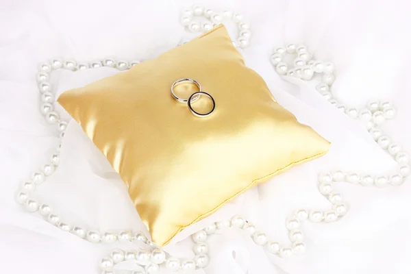 Wedding rings on satin pillow on white cloth background