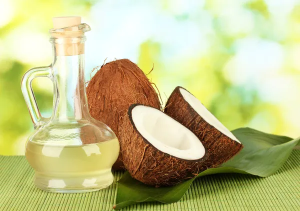 Decanter with coconut oil and coconuts on green background