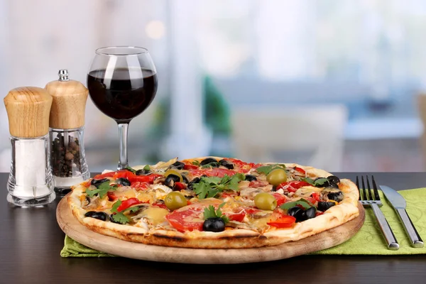 Delicious pizza with glass of red wine and spices on wooden table on room b