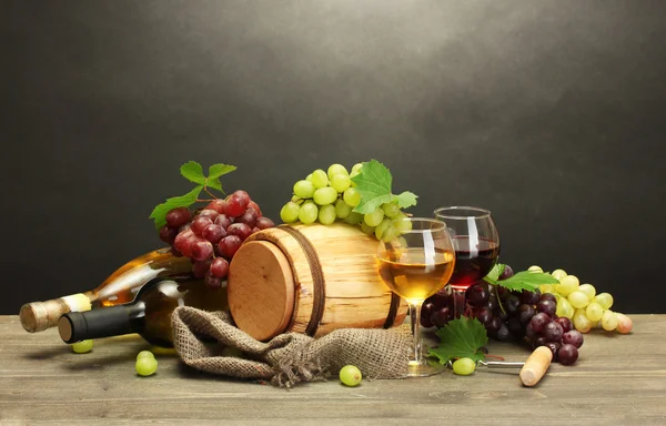 Barrel, bottles and glasses of wine and ripe grapes on wooden table on grey