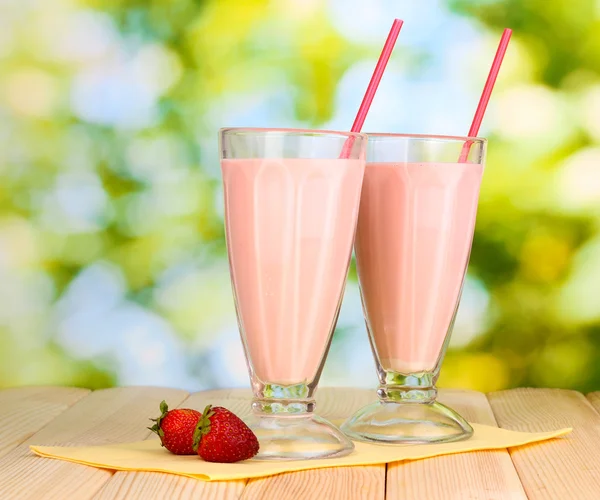 Strawberry milk shakes on wooden table on bright background