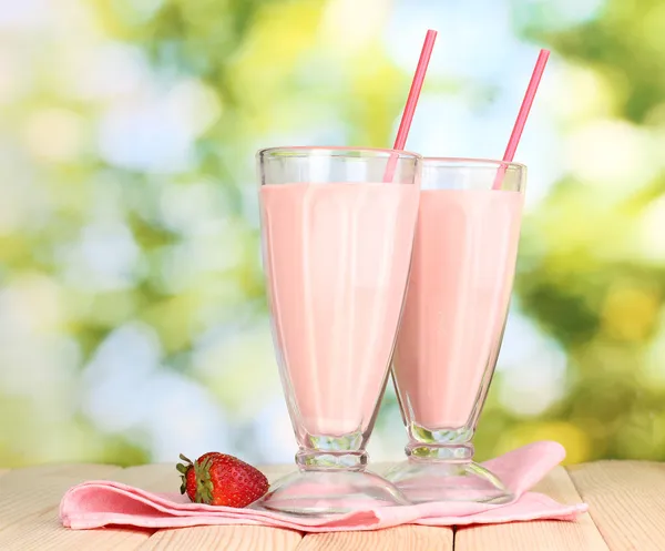 Strawberry milk shakes on wooden table on bright background